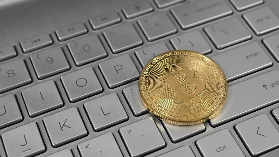 Moeda de bitcoin apoiada sobre o teclado de um notebook